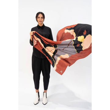 A model is holding out a silk scarf printed with artwork in shades of brown.