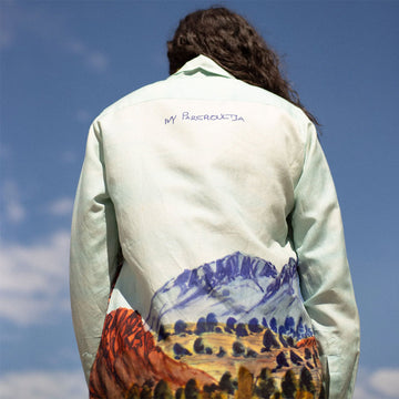 Woman standing against a clear blue sky wearing a light-colored shirt with a floral pattern.