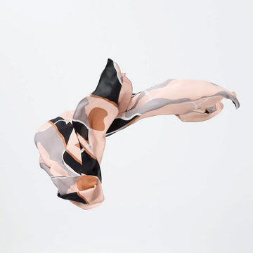 A silk scarf in light pink, grey and brown is half folded up and half floating.