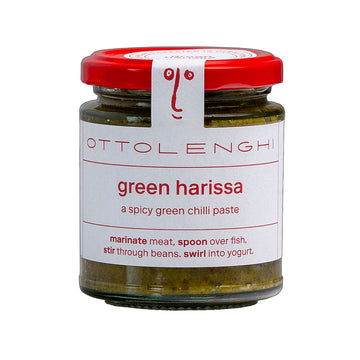 A jar filled with green chilli paste with a white product label on the front with the text 'Green Harissa'.