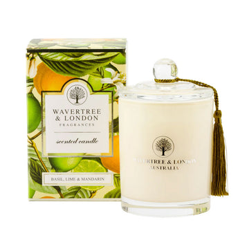 A glass candle next to a box printed with mandarins and limes with basil leaves. Both the box and the candle have a heading 'Wavertree and London'.