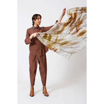 A woman is holding out a silk scarf printed with brown leaves.