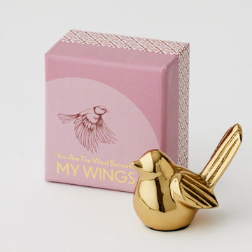 A gold statue of a bird next to a pink box with the text 'You Are the Wind Beneath My Wings' on the box.