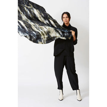 A woman is standing and holding out a silk scarf with a black and grey print.