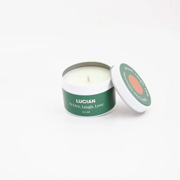 A candle in a small tin with a green label around the edge with the text 'Lucian O'live, laugh, love'.