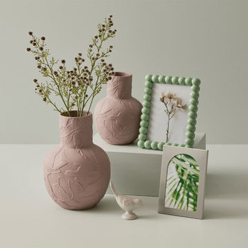A dusty pink porcelain vase with a round base and cylinder top embossed with flowers.