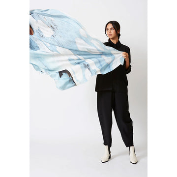 A woman is holding out a silk scarf printed with a light blue and white design.