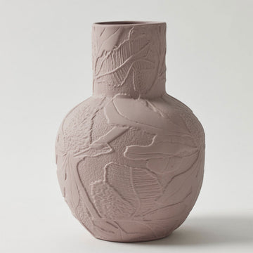 A dusty pink porcelain vase with a round base and cylinder top embossed with flowers.