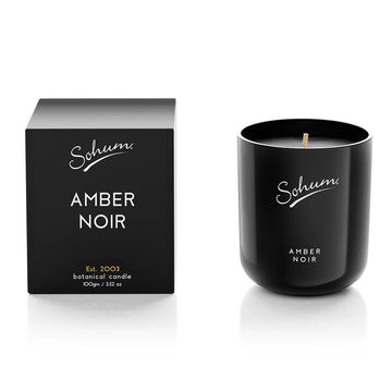 A black glass candle next to a matching black cube box with the text 'Amber Noir' on the front.