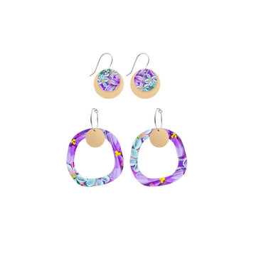 Two pairs of circular earrings printed with blue and purple floral artwork on a hoop and hook.