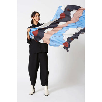 A woman is holding out a silk scarf printed with artwork in blue, white, light brown and black.