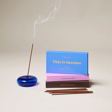 A round glass incense holder in blue with an incense stick in the middle.