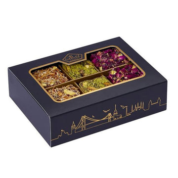 Navy blue box with gold accents containing assorted dried flowers and herbs on top of Turkish delight squares.