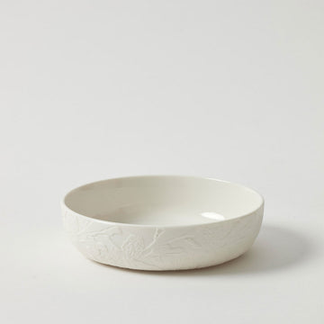 A shallow white porcelain bowl embossed with flowers on the outside.