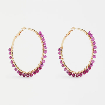 A pair of gold hoop earrings with mulberry pink purple beads around the edges.