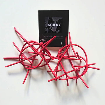 A pair of rubber earrings in red featuring circles and lines in an abstract shape attached to a black card.