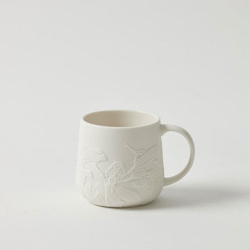 A white porcelain mug embossed with flowers on the outside.