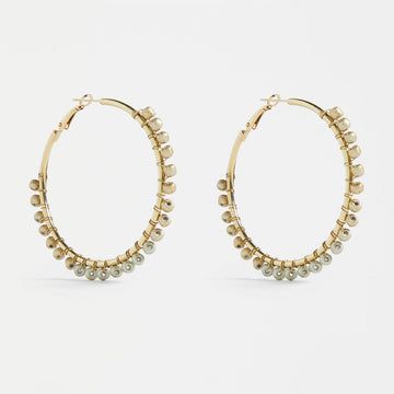 A pair of gold hoop earrings with gold beads around the edges.