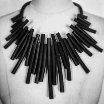 A black rubber necklace made up of thin strips in an abstract shape.