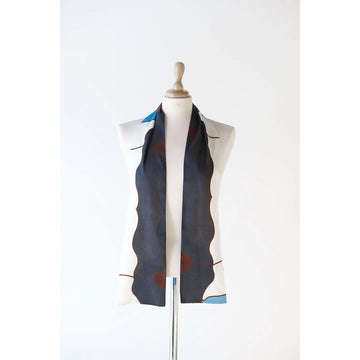 A silk scarf is draped over the shoulders of a mannequin. The scarf is printed with artwork in dark blue, white and brown.