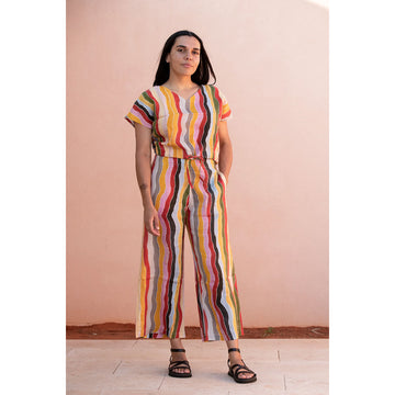 Front view of a woman wearing a colorful striped top and pants against a pink wall.