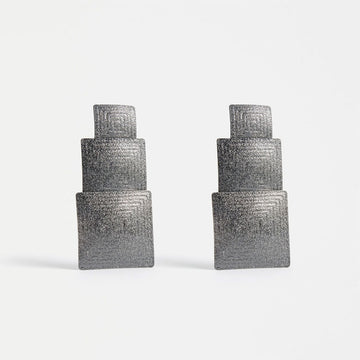 A pair of earrings featuring three different sized gunmetal grey squares.