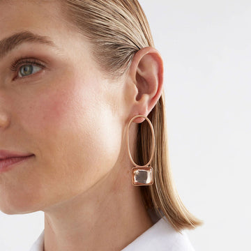 A pair of drop earrings with a hollow oval shaped and a rectangle gem at the bottom, all in the same champagne colour.