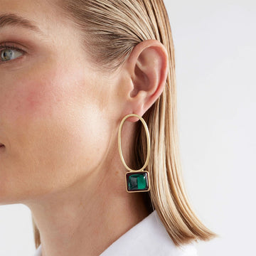 A pair of drop earrings with a hollow oval shaped and a rectangle gem at the bottom, in gold and emerald.