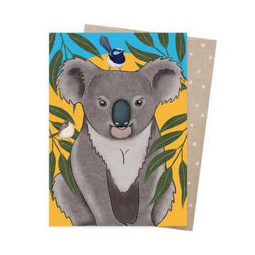 A greeting card illustrated with a fairy wren bird on a koala's head surrounded by gum leaves.
