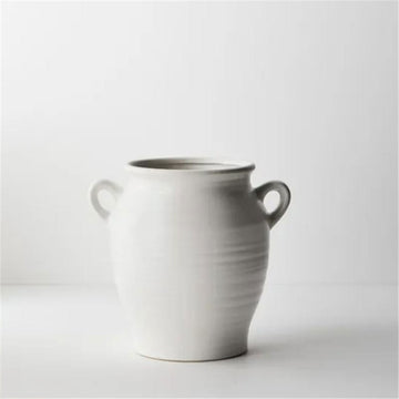 A white ceramic vase in a tall round shape with little round handles on either side.