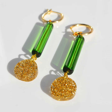 A pair of gold hoop earrings with a long green bead and gold glitter circle attached to the hoop.