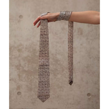 A silk tie in light brown printed with a line design in a darker brown by Ray James Tjangala.