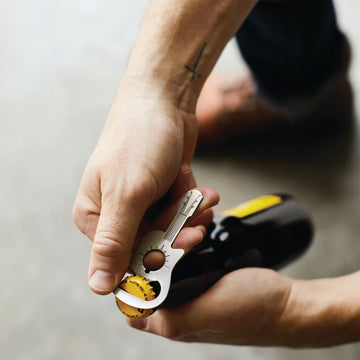 A guitar shaped bottle opener in stainless steel attached to a green and brown card.