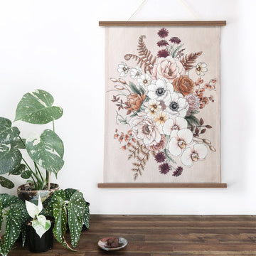 A folded up tea towel in beige illustrated with large flowers in white, light pink and yellow. There is a white sleeve around the tea towel with product information.