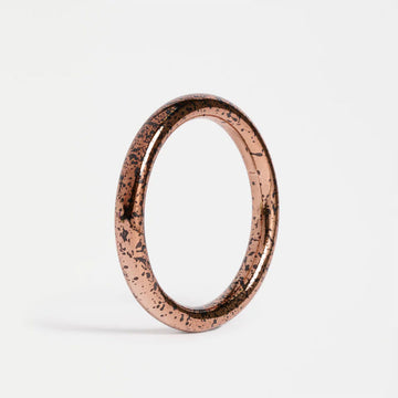 Rose gold bangle with speckles on a light grey background.