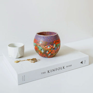 Decorative candle holder with colorful patterns next to its packaging box on a white background.