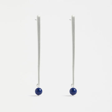A pair of stud drop earrings with a long narrow bar in silver with a dark blue round bead on the end.