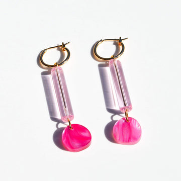 A pair of gold hoop earrings with a long light pink bead and pink marble circle attached to the hoop.