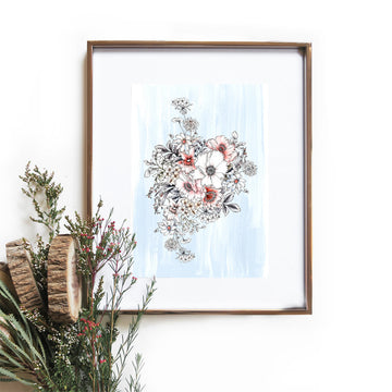 An illustrated bouquet of flowers on a pale blue background inside a gold frame hanging on a wall with a bunch of flowers in front.