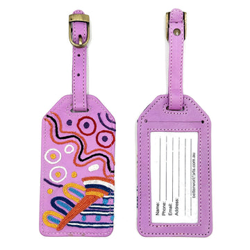 Front and back view of a purple luggage tag. The front is embroidered with artwork by Andrea Adamson and the back has a clear sleeve with personal details.