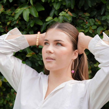 A pair of gold hoop earrings with a long light pink bead and pink marble circle attached to the hoop.