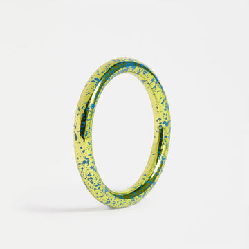 Yellow bangle with blue speckles on a light gray background.