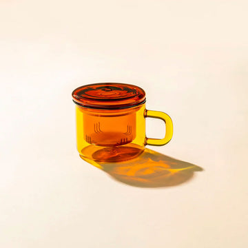 Amber-colored glass mug with a matching lid on a beige background.