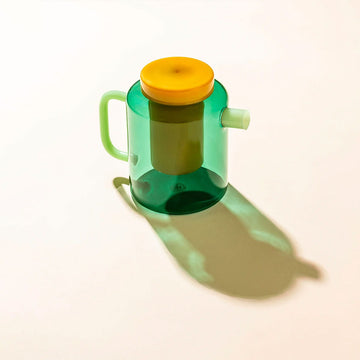 Green glass pot with a yellow lid and infuser on a white background.