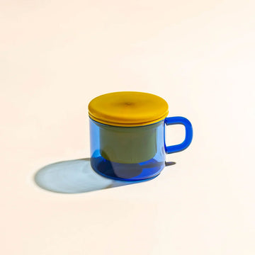 A glass mug in blue with a yellow lid and infuser inside.