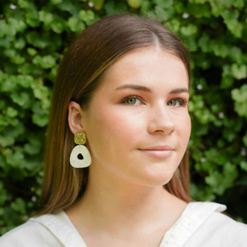 A pair of drop earrings with a gold glitter square on top and a pearl white circle on the bottom.