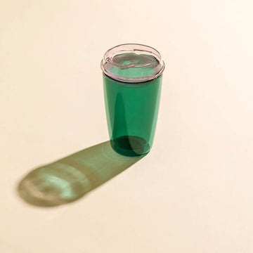 Green glass travel mug with a clear lid on a beige background.