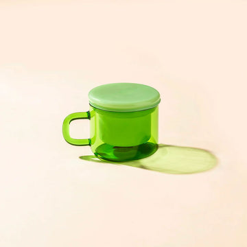 Green mug with a matching lid on a beige background.