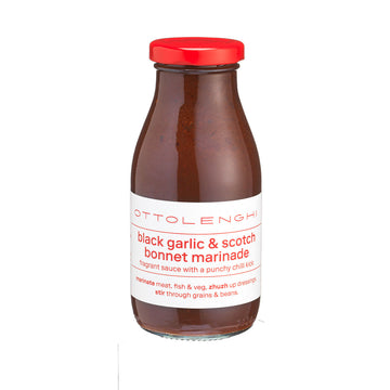 Bottle of black garlic & scotch bonnet marinade with a red cap on a white background.