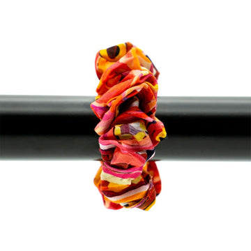 Colorful scrunchie on a black bar with a white background.